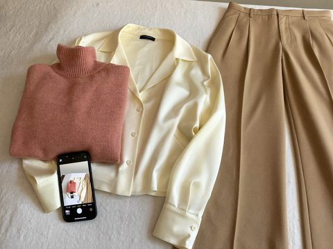 A rose turtleneck, ivory blouse and camel trousers laid out beside a phone