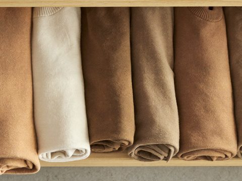 Rolled knitwear lined up by colour on a wooden shelf