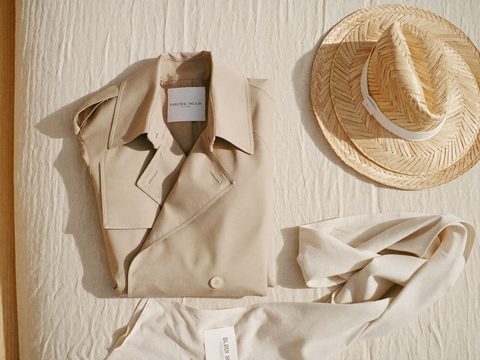 A trench coat, straw hat and light scarf laid out on linen